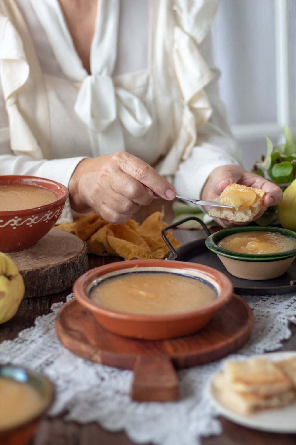Marmelada servida em taças de barro, à mesa, com pão e marmelos